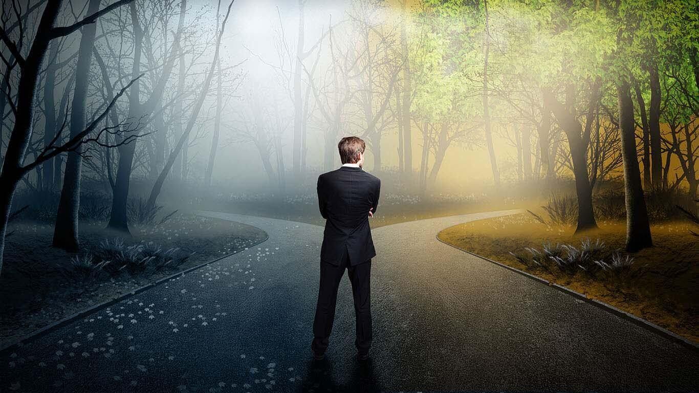 Person an einer Weggabelung im Wald – ein dunkler und ein lichter Weg
