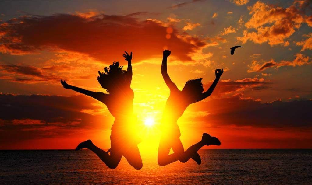 Zwei Menschen springen vor Freude in den Sonnenuntergang am Meer